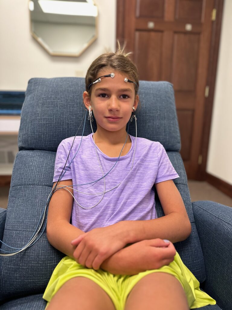 Child undergoing a neurofeedback session, wearing EEG sensors and focusing on a computer screen, demonstrating natural ways to calm ADHD in kids