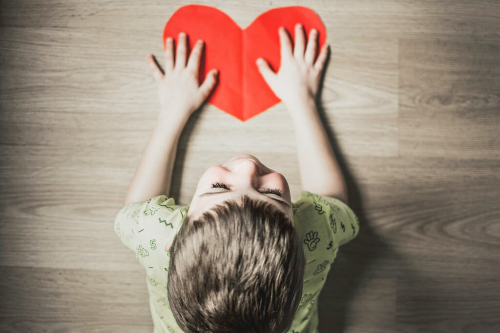 A child sitting on the floor holding a heart cut-out, symbolizing emotional healing through alternative treatment for attachment disorder